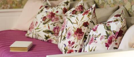A bed with floral-patterned pillows and a book on a pink bedspread.