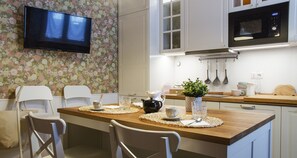 A modern kitchen with a wooden island, white chairs, a flat-screen TV, and a microwave.
