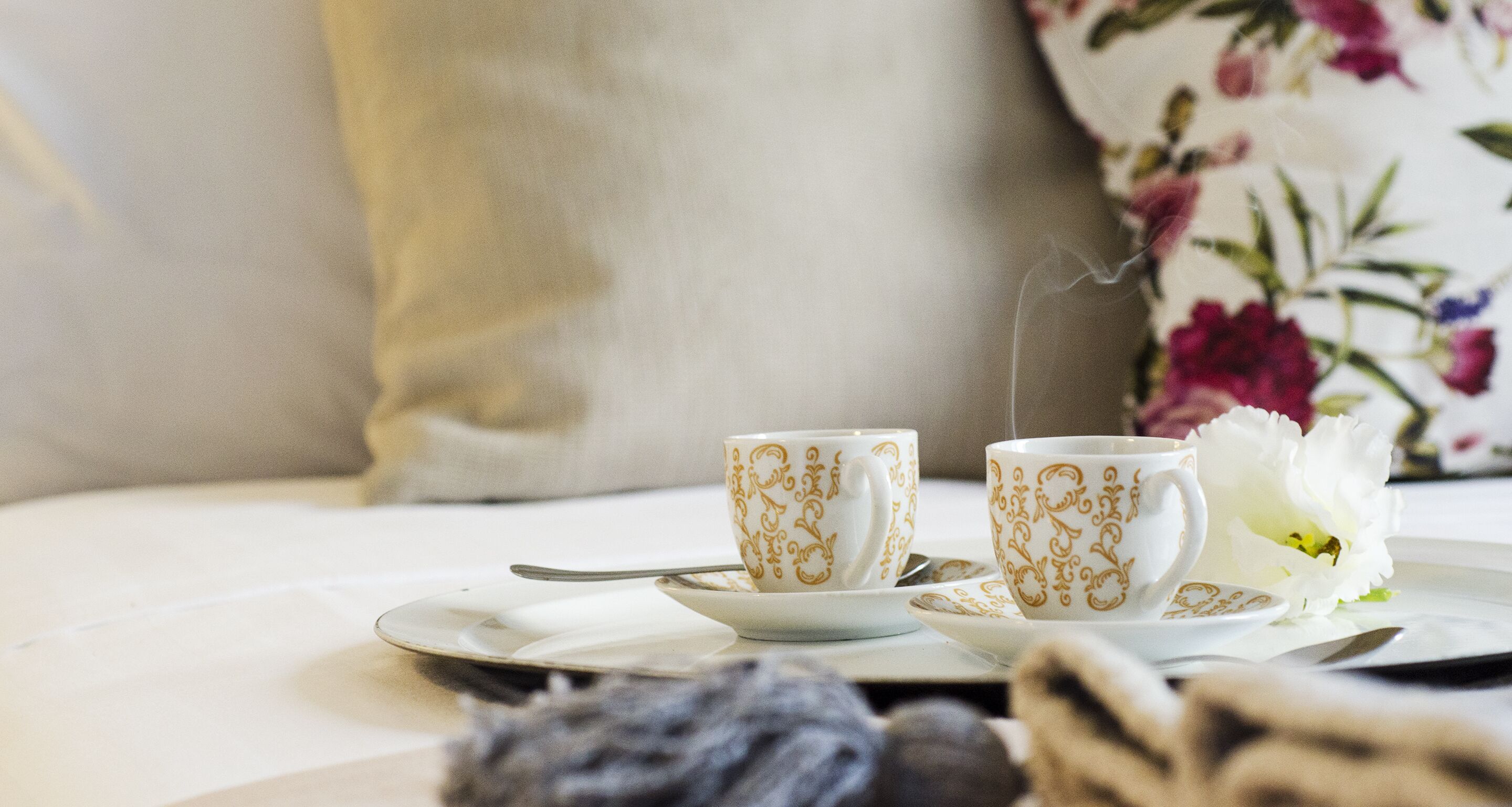A table with two white cups with gold patterns, a spoon, and a plate.