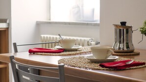 A dining table with two white cups and saucers, a red napkin, and a silver coffee pot. - JOIVY Little House (Como)