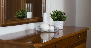 A wooden dresser with a mirror, a glass vase with a plant, and a glass bowl with two white candles. - JOIVY Little House (Como)