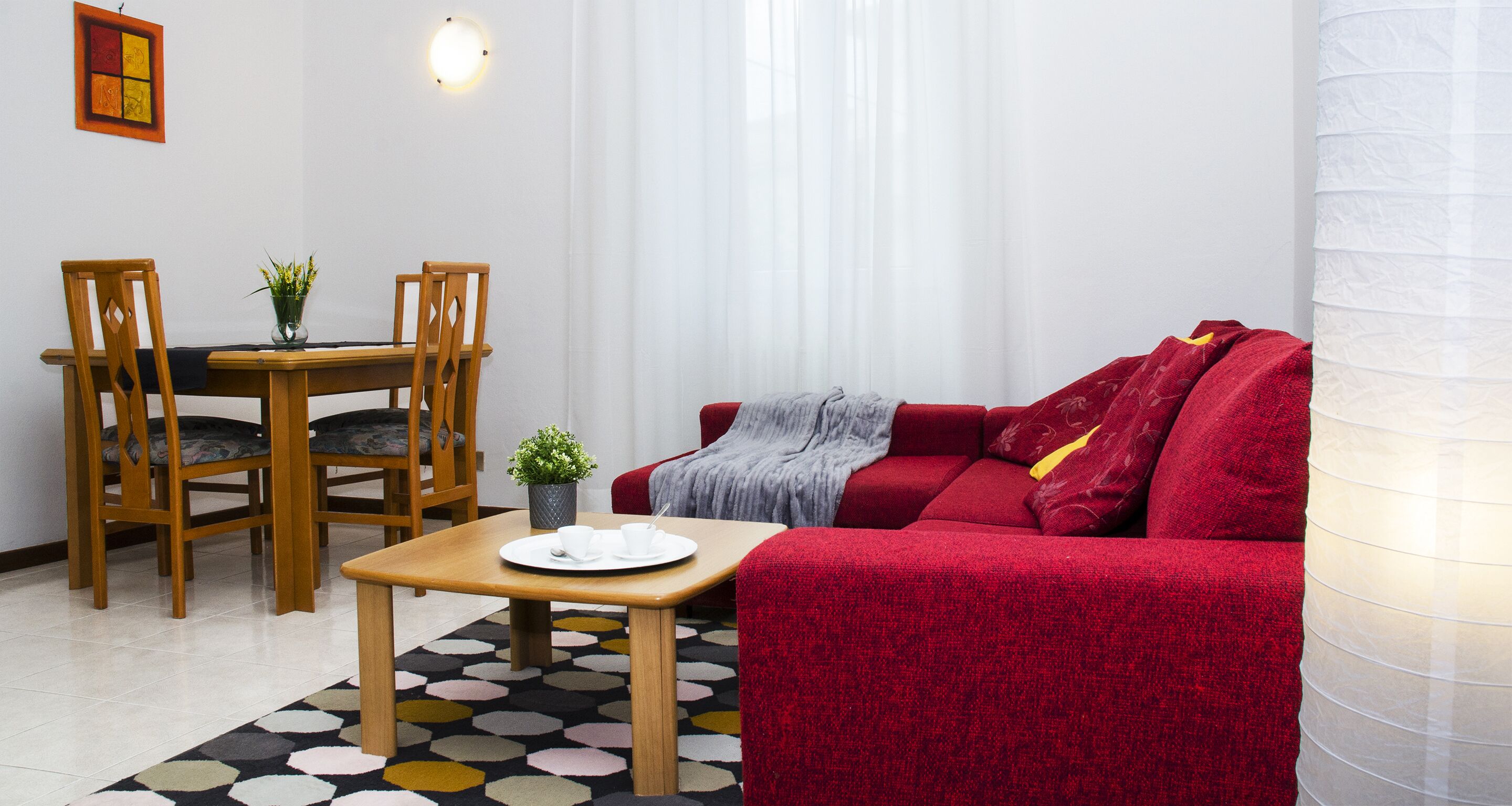Ein Wohnzimmer mit einem roten Sofa, Holzstühlen, einem kleinen Tisch mit Tablett und einer Topfpflanze.