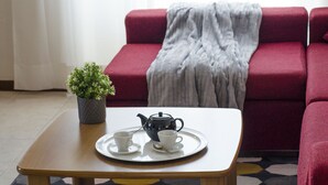 A room with a wooden coffee table, two white cups, a teapot, and a tray. There is a red sofa with a grey blanket and a small potted plant on the table. - JOIVY Little House (Como)