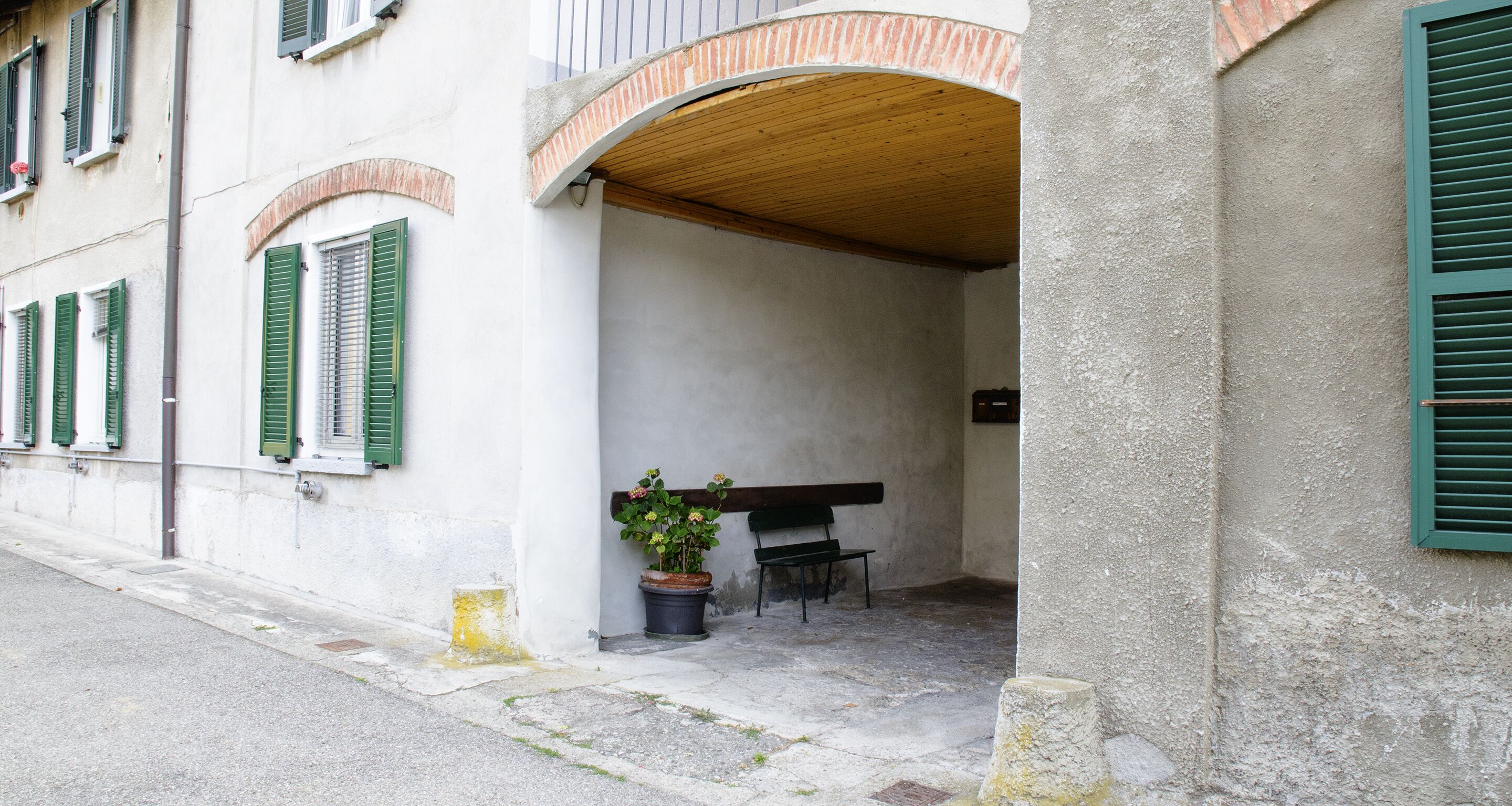 A building with a covered entrance, a bench, and a potted plant.