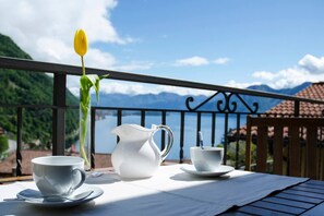 A table with a white pitcher, two white cups, and a yellow tulip on a balcony overlooking a lake and mountains. - JOIVY Attic on the Lake (Argegno)