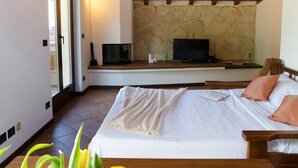 A bedroom with a bed, a stone wall, a television, and a small table with a book and a vase. - JOIVY Attic on the Lake (Argegno)