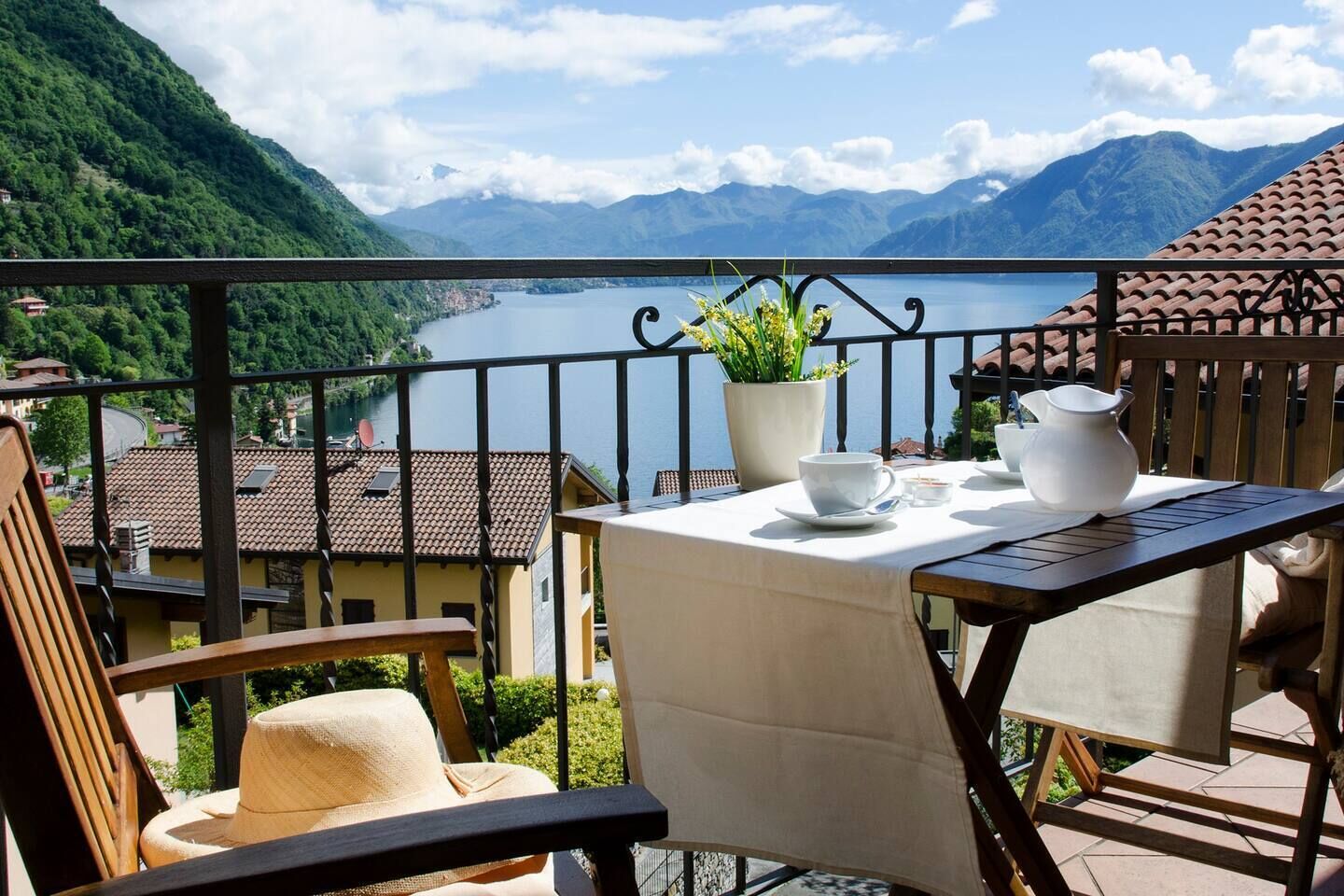 A balcony with a table set for two, overlooking a lake and mountains.