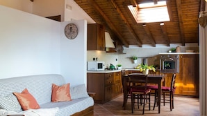 A cozy living room with a checkered sofa and a dining area with wooden chairs and a table. A kitchen with wooden cabinets and a stove is visible in the background. - JOIVY Attic on the Lake (Argegno)