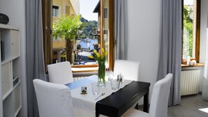 Un comedor con una mesa preparada para dos, vista a un pueblo y una masa de agua, y una ventana con cortinas.