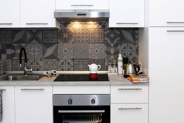 A modern kitchen with white cabinets, a stainless steel sink, a built-in oven, and a patterned backsplash.