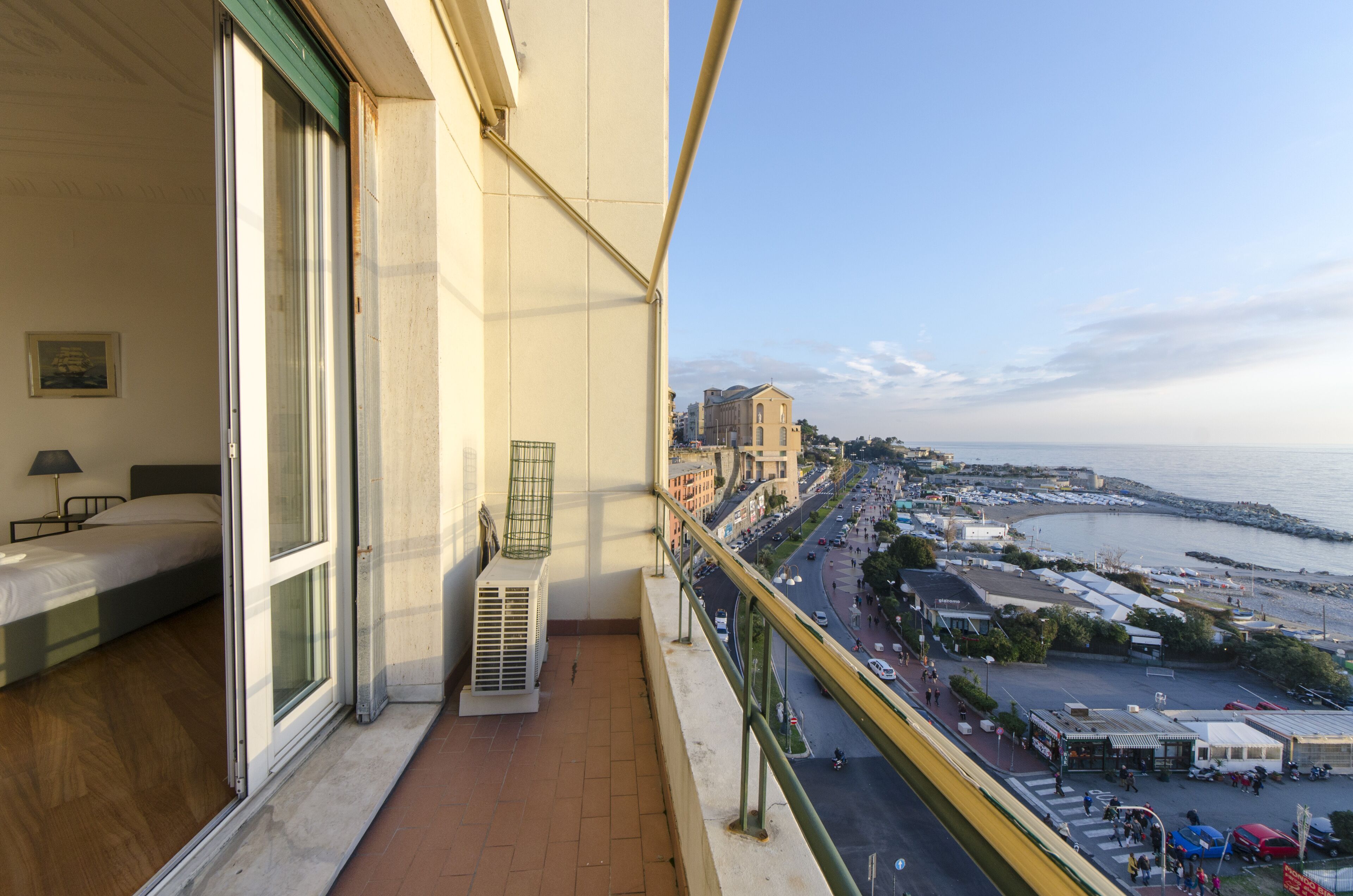 A balcony with a view of a coastal town, a bed, and an air conditioning unit.