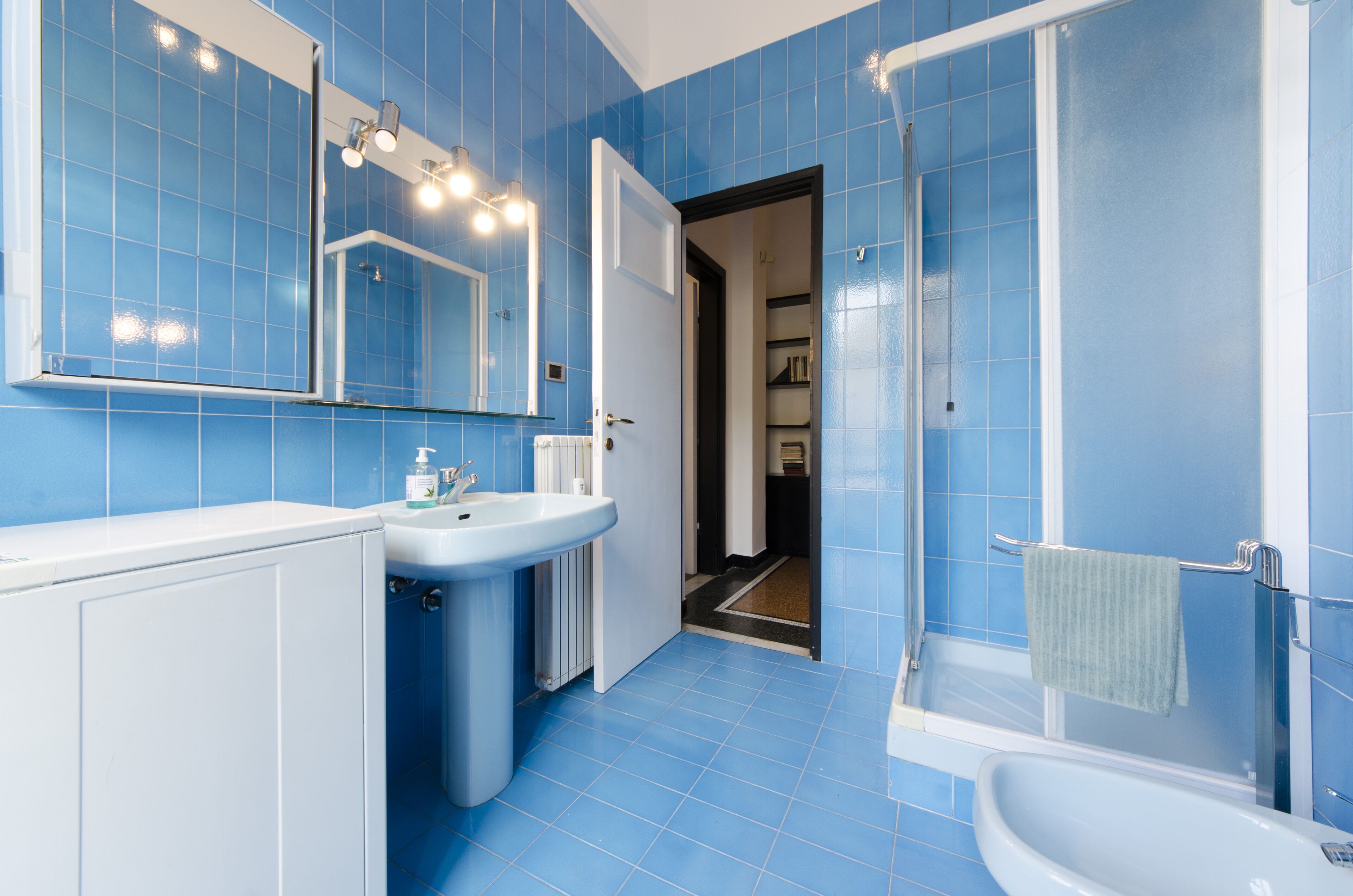 A bathroom with blue tiles, a white sink, a mirror, and a shower area.