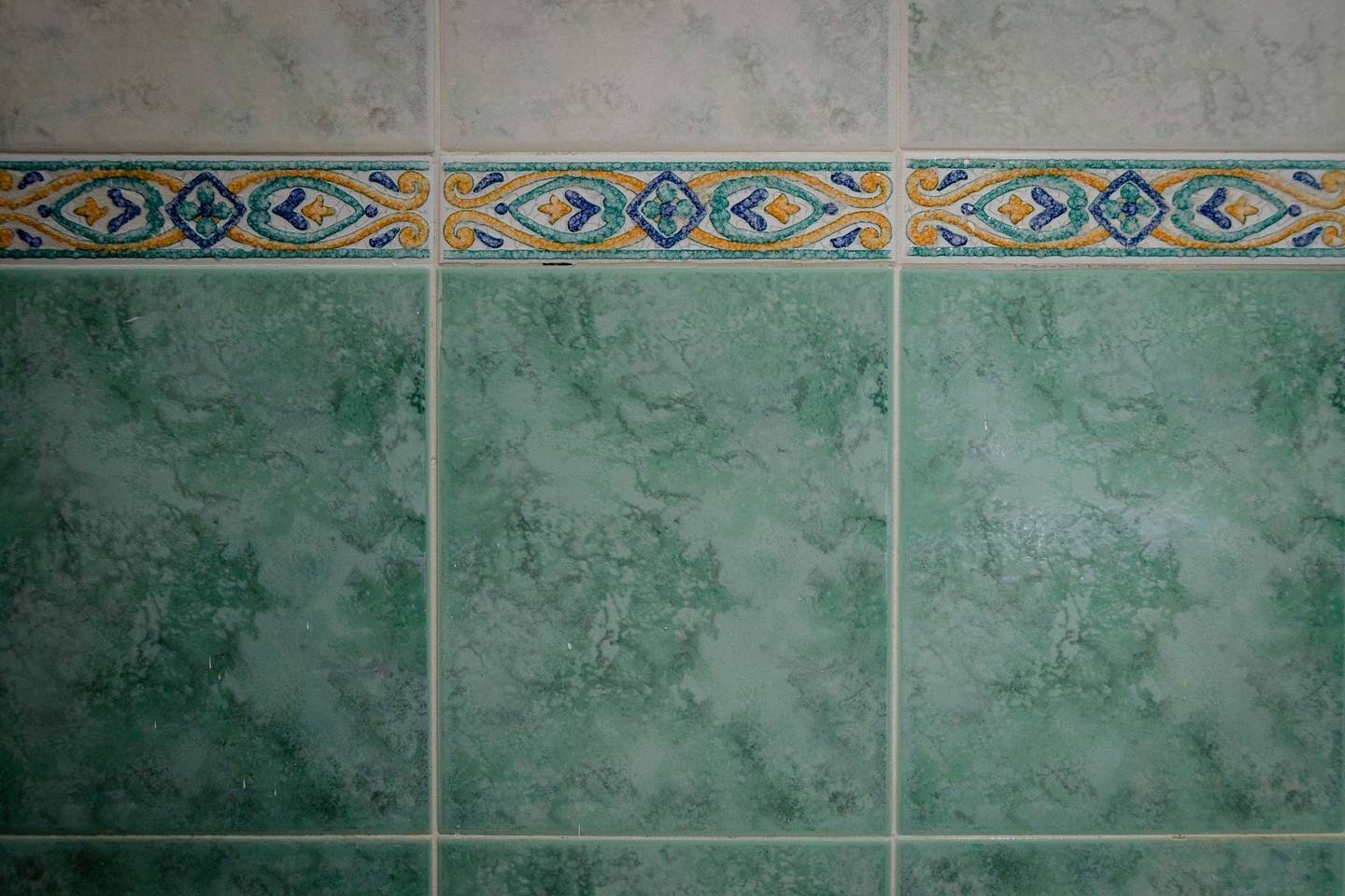 Une partie d’un mur recouverte de carreaux verts, agrémentée d’une bordure décorative.