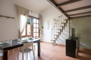 A dining area with a table set for four, a staircase with a unique design, and a television on a stand. - JOIVY Green Terraced House (Pisa)