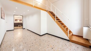A spacious hallway with a wooden staircase and a polished terrazzo floor.
