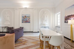 Una sala de conferencias moderna con una mesa blanca, sillas y un sofá. Hay tres estatuas blancas en las paredes, un cuadro de un barco y una lámpara a la derecha.