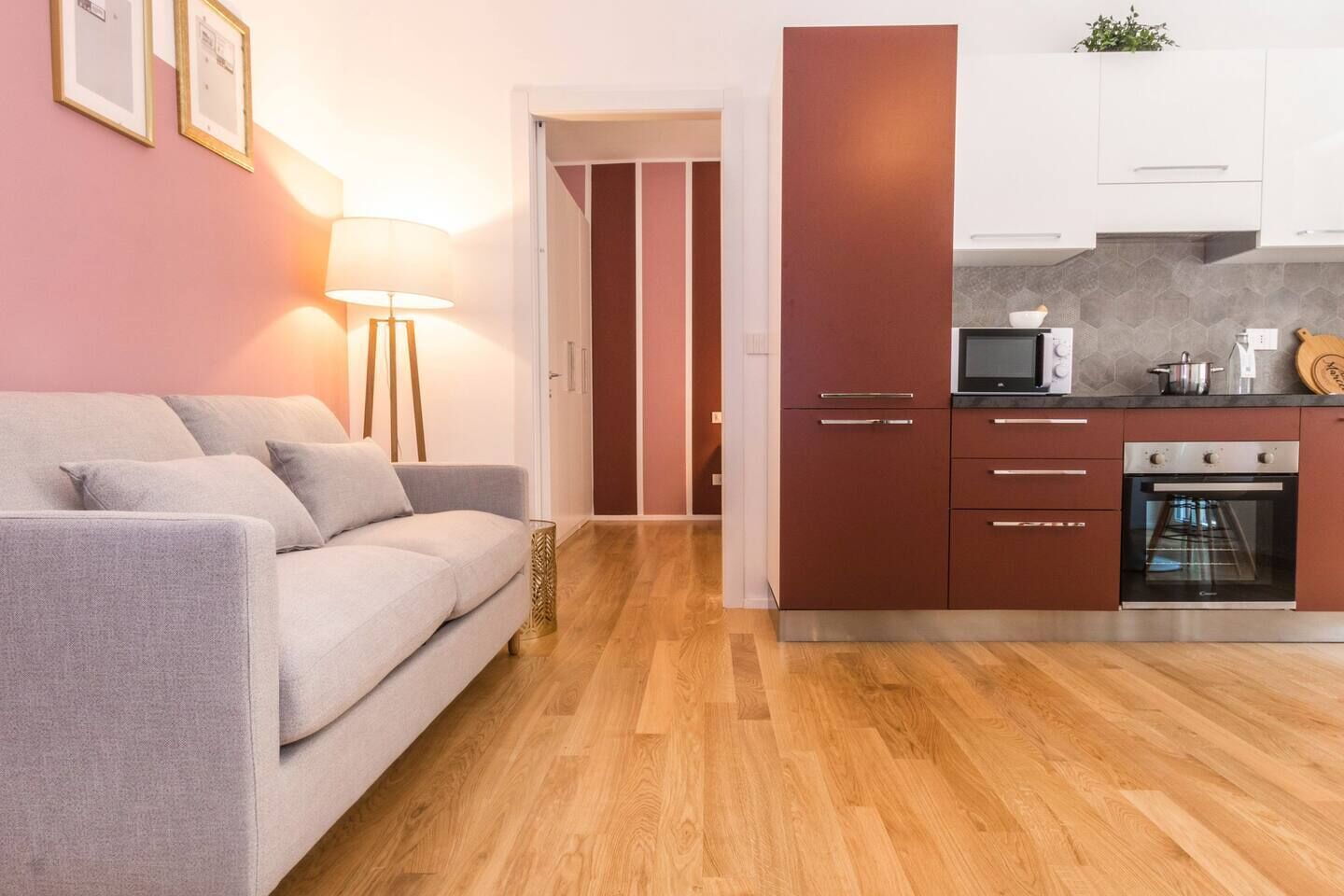 A modern apartment with a grey sofa, wooden flooring, a kitchen with white cabinets, and a microwave.