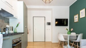 A modern kitchen with a built-in oven, a dining area with a table and chairs, and a flat-screen TV mounted on the wall. - JOIVY Lotto Square Apartment (Milan)
