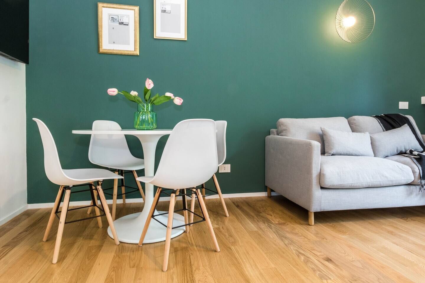 Un soggiorno moderno con una parete verde, un divano grigio, un tavolo da pranzo bianco con quattro sedie e un vaso con fiori.