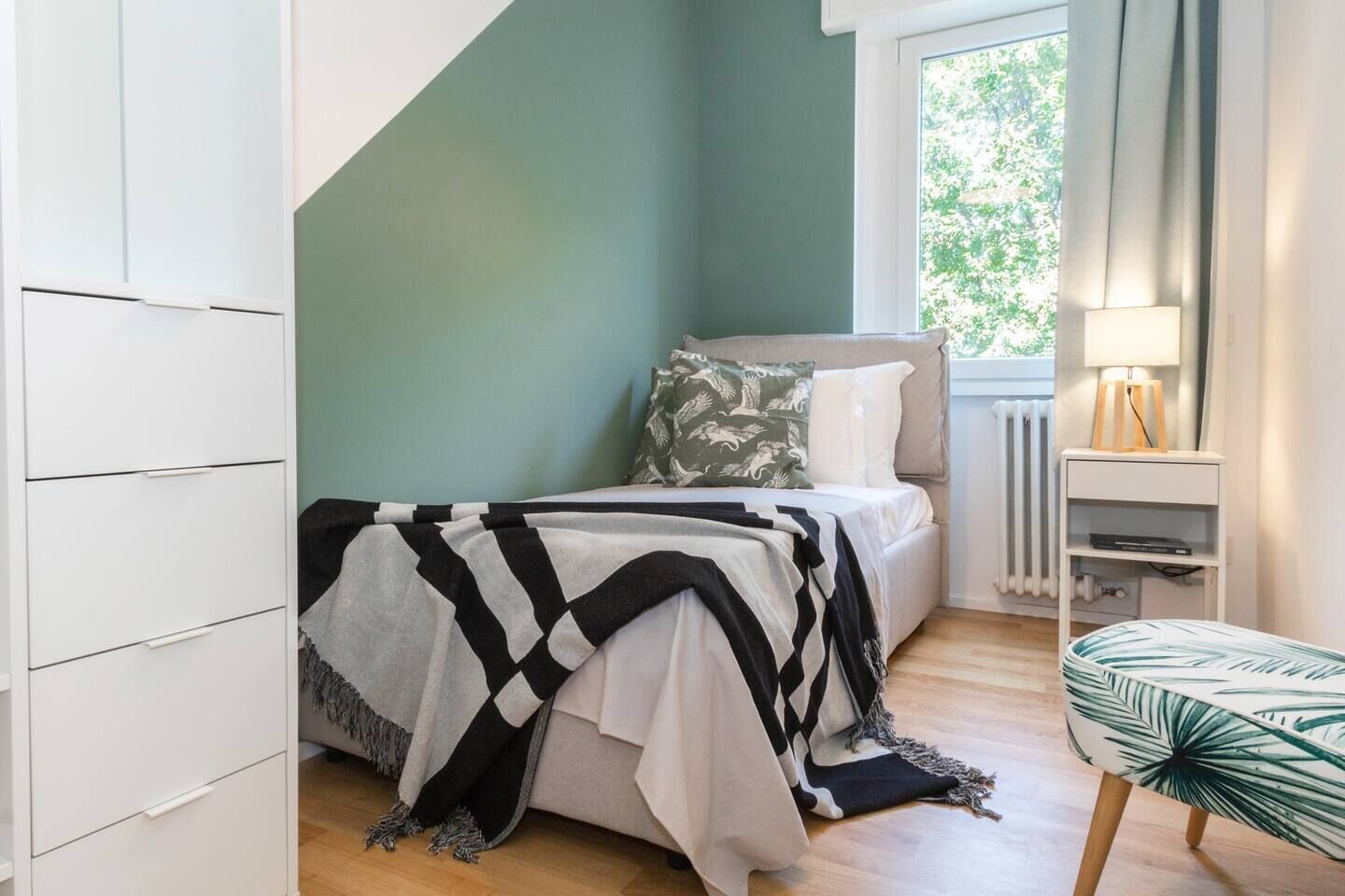 A bedroom with a bed, a bedside table, a chair, and a window with curtains.