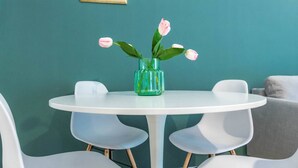 A round white table with a green vase containing pink flowers, surrounded by white chairs. - JOIVY Lotto Square Apartment (Milan)