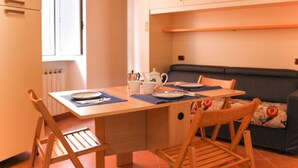 A dining area with a table set for two, chairs, a sofa, and a radiator in the background. - JOIVY Riva Trigoso Casetta nel Borgo (Sestri Levante)
