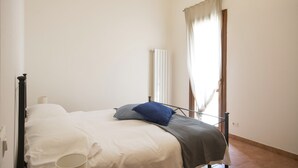A bedroom with a bed, a radiator, and a window with curtains. - JOIVY Red Terraced Apartment (Pisa)