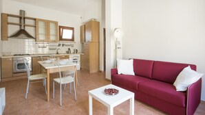 A modern kitchen with wooden cabinets, a dining area with a white table and chairs, and a red sofa in a living area. - JOIVY Red Terraced Apartment (Pisa)