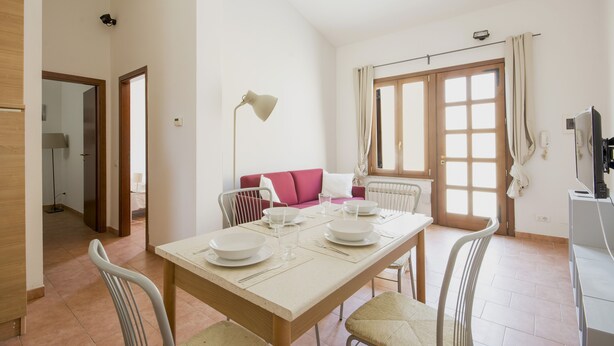 A dining area with a table set for four, a red sofa, and a window with curtains. - JOIVY Red Terraced Apartment (Pisa)