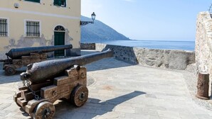 A coastal fortification with cannons, a stone wall, and a building with green shutters. - JOIVY Porto Bello a Camogli (Camogli)