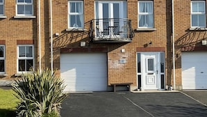 A two-story brick building with a garage door, a small balcony, and a chimney. - The Green, Portrush. Deluxe holiday home, 8 beds 12 guests 5 bedrooms. (Portrush)