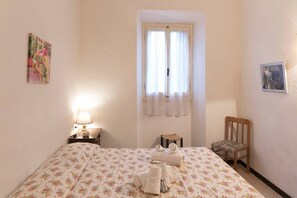 A bedroom with a bed, a chair, a nightstand, a lamp, a window with curtains, and a painting on the wall. - JOIVY Villa Il Glicine sul Mare (Pietrasanta)