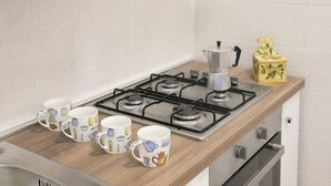 A kitchen with a gas stove, four coffee mugs, a coffee pot, and a decorative box. - JOIVY Villa Il Glicine sul Mare (Pietrasanta)