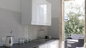 Una cocina moderna con armarios blancos, un lavamanos de acero inoxidable y un balcón con mobiliario de mimbre.