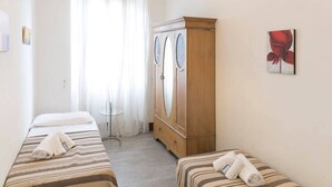 Una habitación de hotel con dos camas individuales, un armario de madera, una mesita pequeña y un cuadro en la pared.