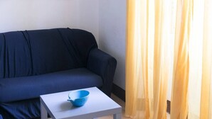 Una habitación con un sofá azul oscuro, una mesita blanca con un tazón azul encima y cortinas amarillas.
