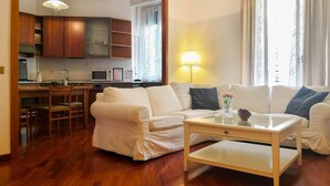 A living room with a white sofa, a coffee table, and a kitchen in the background. - JOIVY Wooden Guerrini Apartment (Milan)