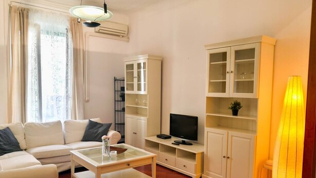 A living room with a white sofa, a coffee table, a TV on a stand, and built-in shelving. - JOIVY Wooden Guerrini Apartment (Milan)