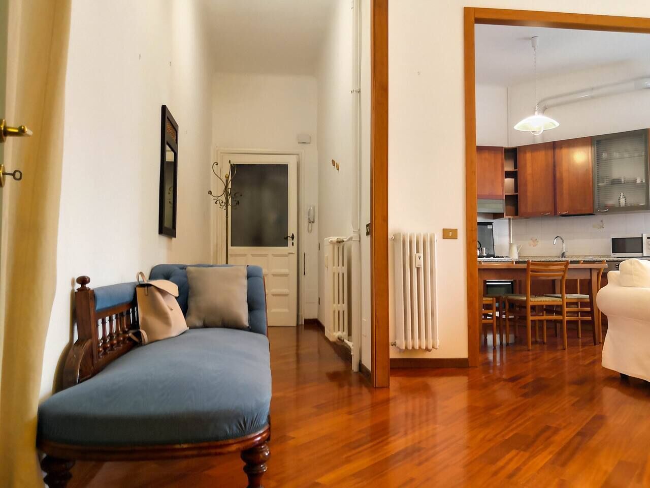 Una stanza con un letto, una sedia, un termosifone e un angolo cottura con mobili e un piano di lavoro.