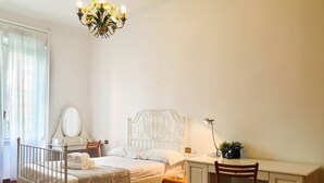 A bedroom with a bed, a desk, a chair, a mirror, and a chandelier. - JOIVY Wooden Guerrini Apartment (Milan)