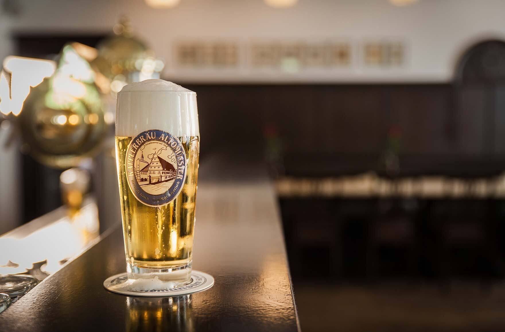 Un vaso alto de cerveza con un logotipo, sobre una barra de bar.