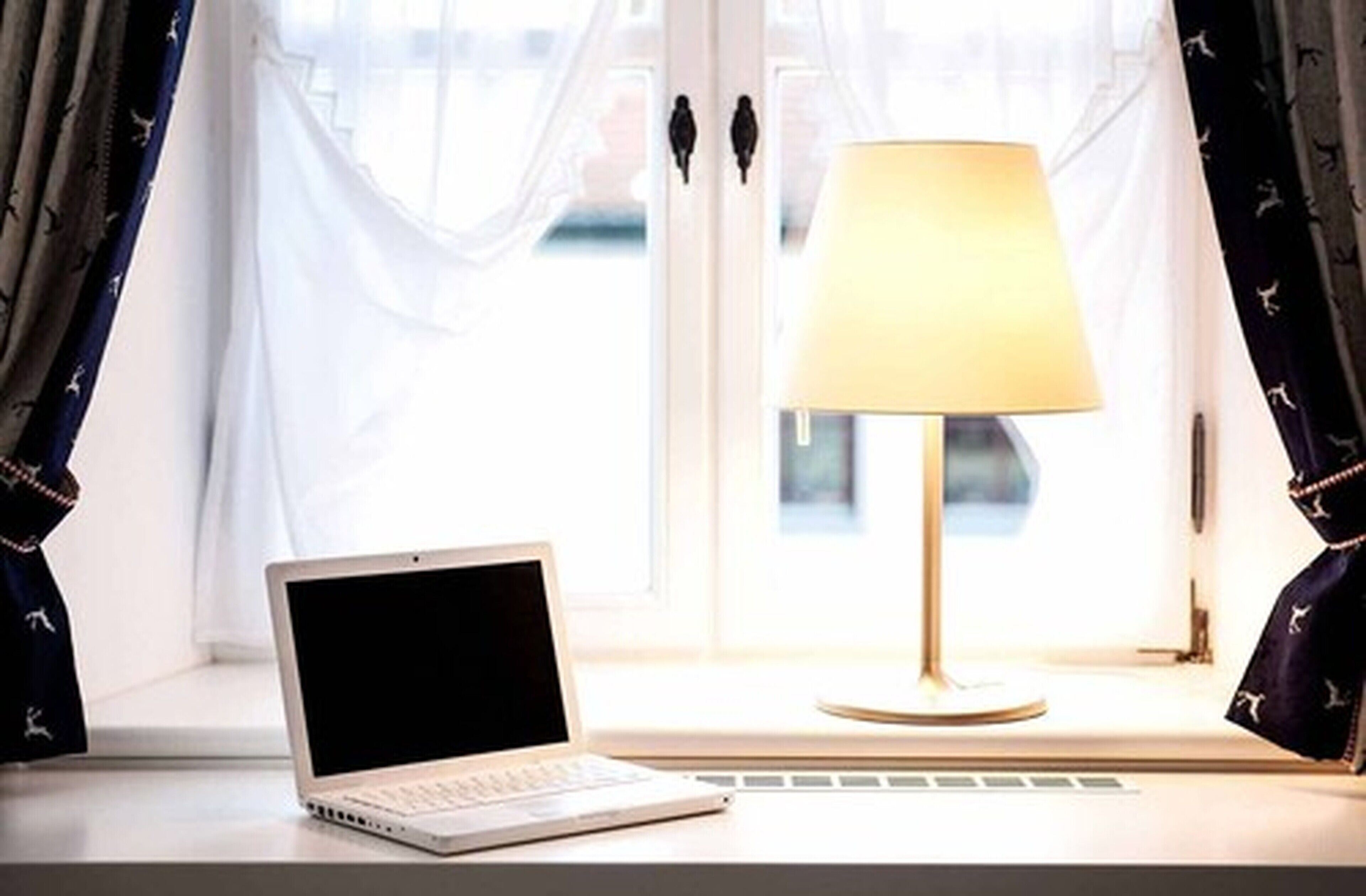 A laptop on a windowsill with a lamp beside it.