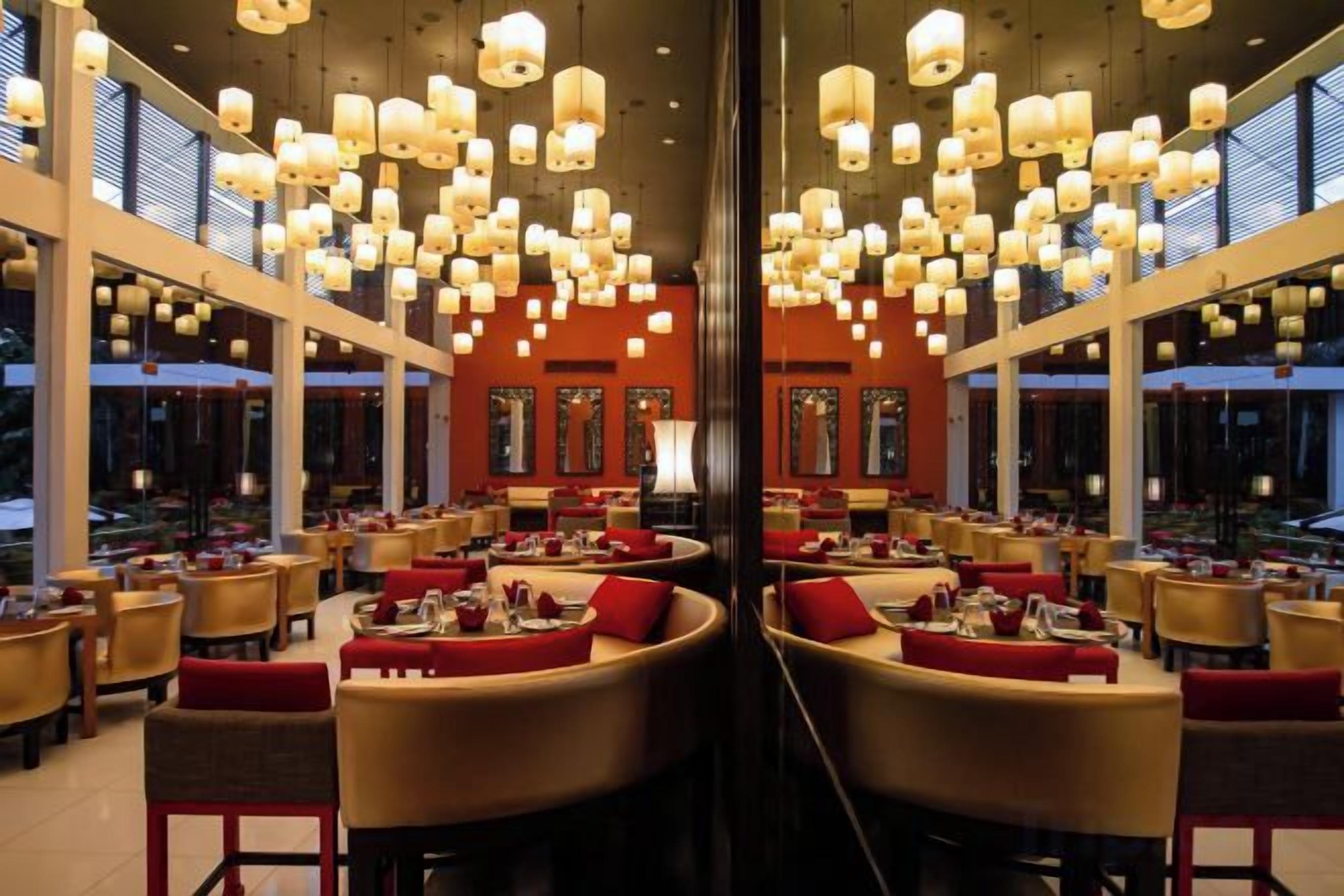 Un restaurant doté de nombreuses tables et chaises, de grandes fenêtres et de luminaires suspendus.