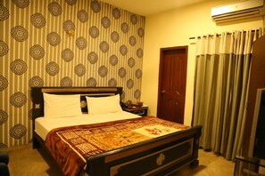 A hotel room with a large bed, a wooden headboard, a patterned wall, a door, and a curtain. - Hotel Sweet Inn (Lahore)