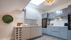 A modern kitchen with white cabinets, a built-in oven, and a large clock on the wall. - 3 Bedroom Apartment in Windermere - Bathtub (Windermere)