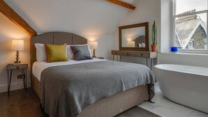 A bedroom with a bed, bedside lamps, a dresser, a mirror, a potted plant, and a view of the outside through a window. - 3 Bedroom Apartment in Windermere - Bathtub (Windermere)