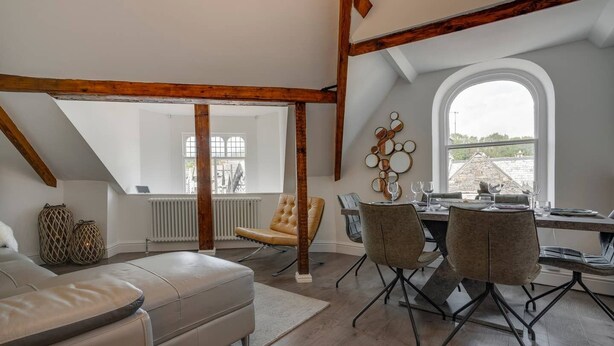 A dining area with a table set for four, a leather sofa, and a window with a view. - 3 Bedroom Apartment in Windermere - Bathtub (Windermere)