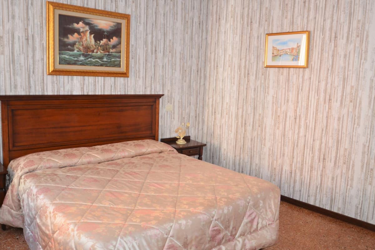 Ein Schlafzimmer mit einem Holzkopfende, einer blumigen Tagesdecke, einem Nachttisch mit Globus und zwei gerahmten Bildern an der Wand.