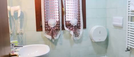 Un baño con dos lavabos, un inodoro, un secador de manos y una ventana con cortinas estampadas.