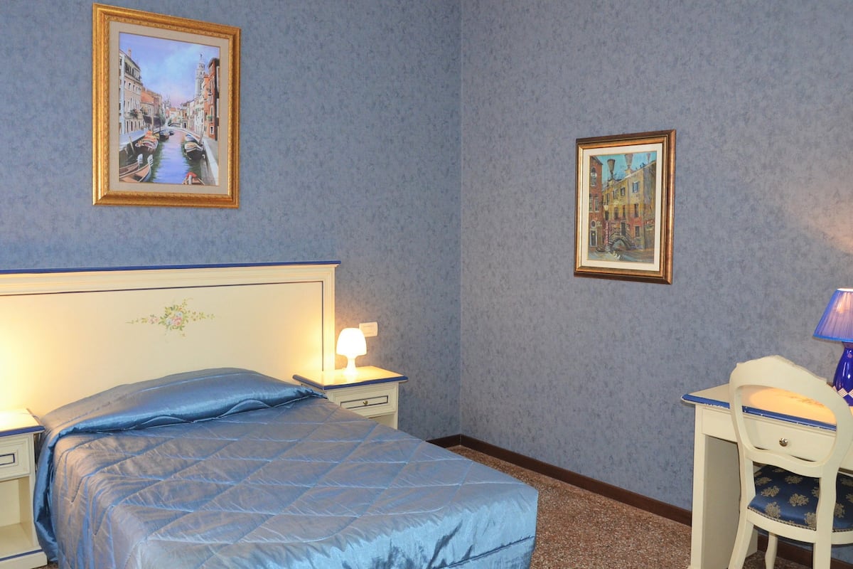 Ein Hotelzimmer mit einem Bett, Nachttischen, einem Schreibtisch und zwei gerahmten Bildern an der Wand.